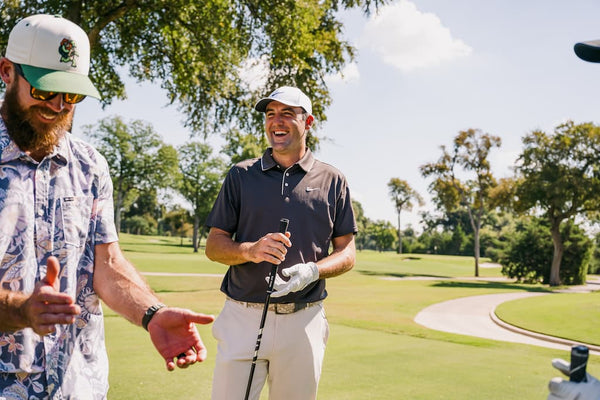 Scottie Scheffler and Jon McKenzie on a golf course with trees and a clear sky in the background