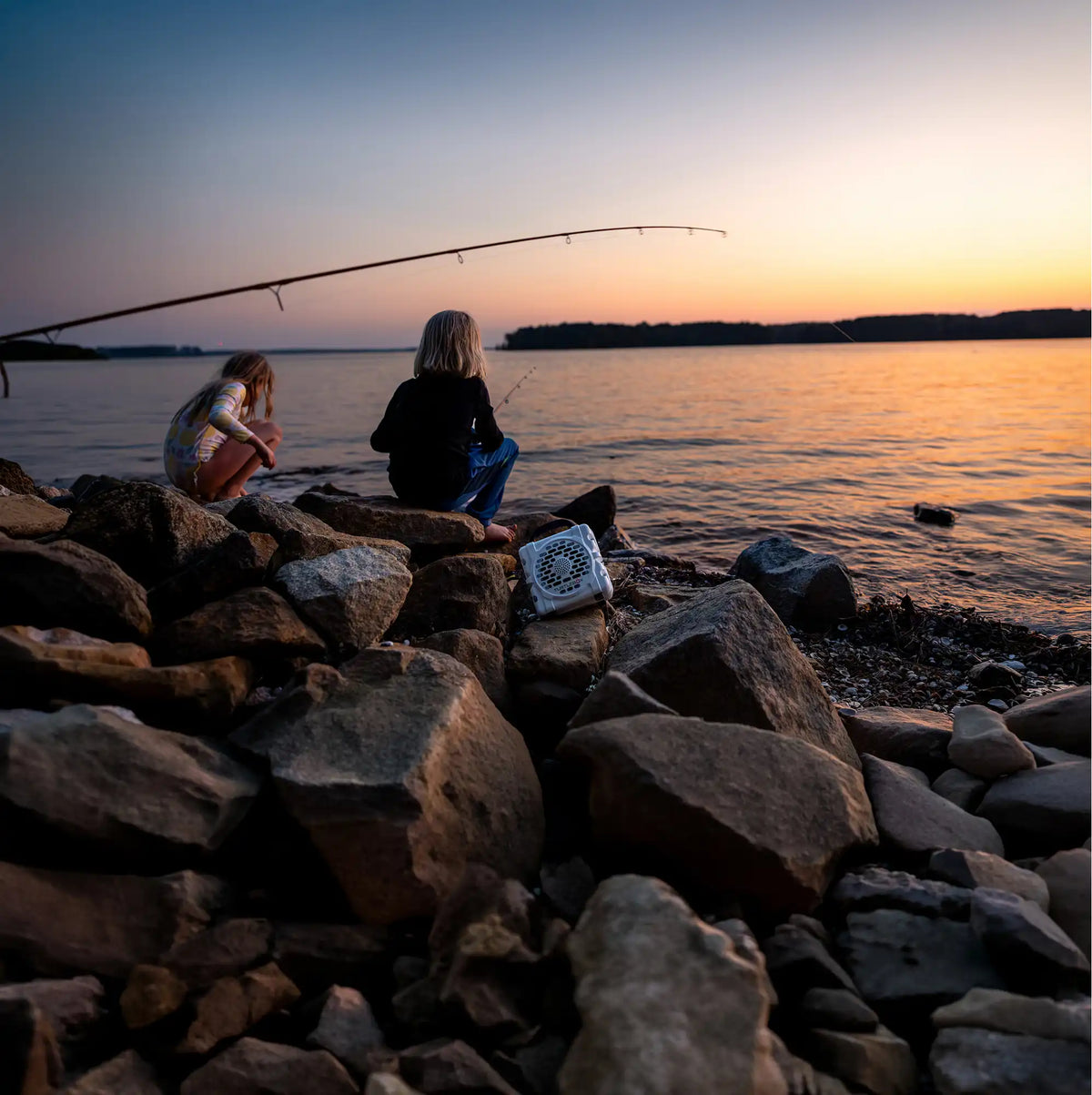 Two people fishing on a rocky shoreline at sunset.