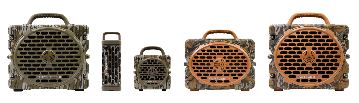 Four camouflage hunting cameras shown in different sizes against a white background, featuring a front speaker grille and top carrying handles.