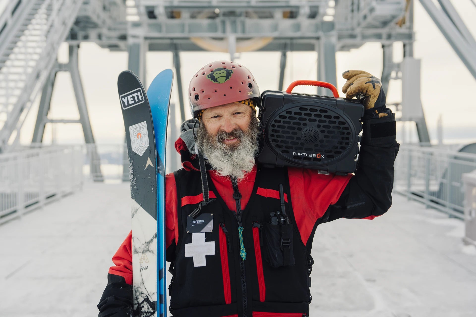 Person in winter gear holding skis and a Yeti cooler in a snowy landscape.
