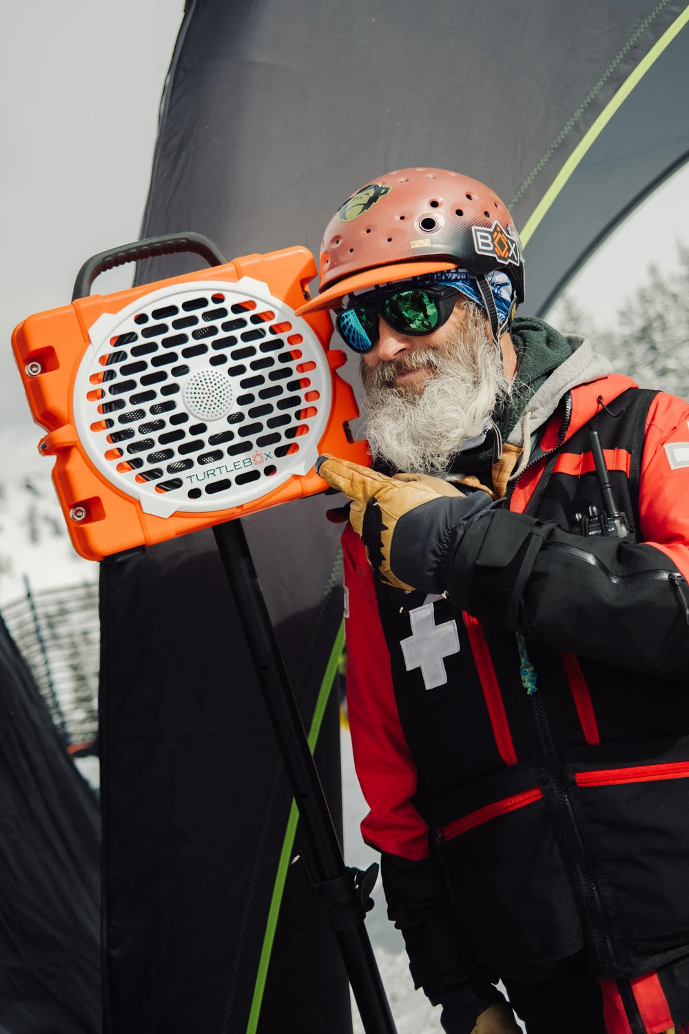 Person in winter gear holding an orange and black device with a helmet and goggles on.
