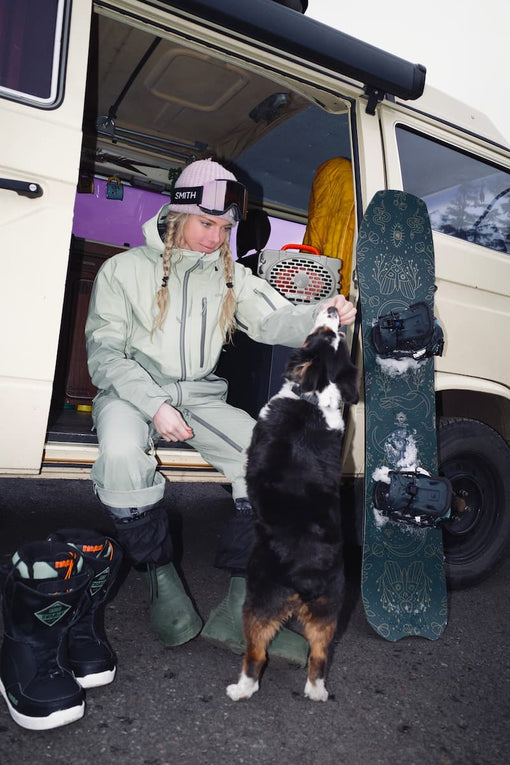 A girl with her dog, a snowboard and the Turtlebox Original speaker in tan color with blaze orange handle