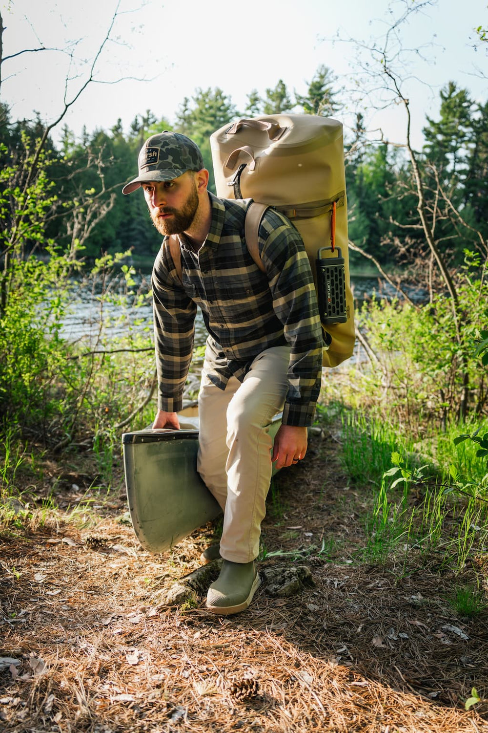 A lifestyle photo from a guy pushing his boat from water and bringing a Ranger speaker in gray attached to his backpack.