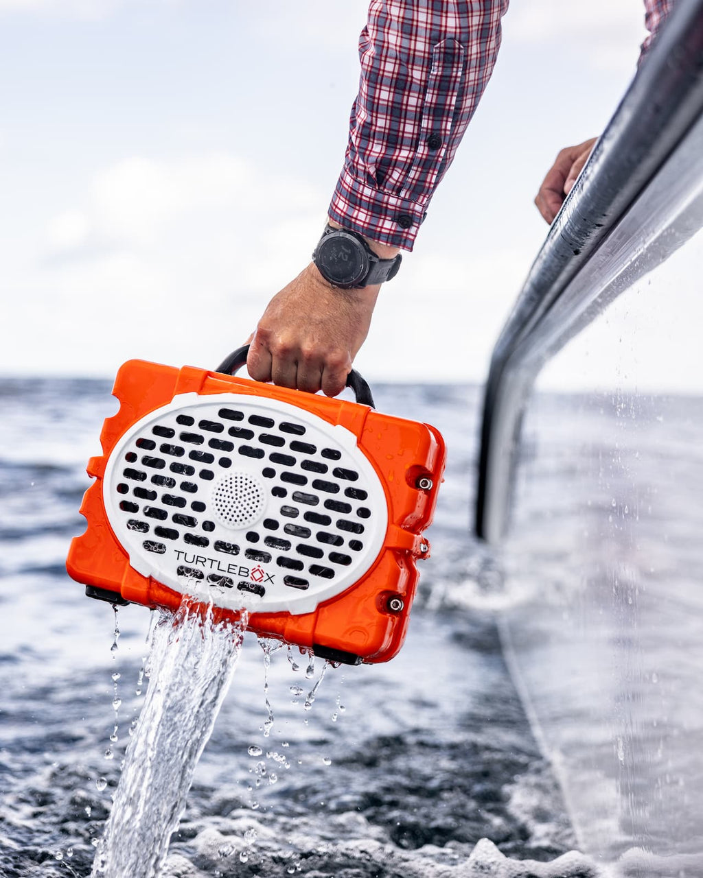A lifestyle photo of a guy in a boat removing Original Gen 3 orange speaker from water #speaker-color_orange