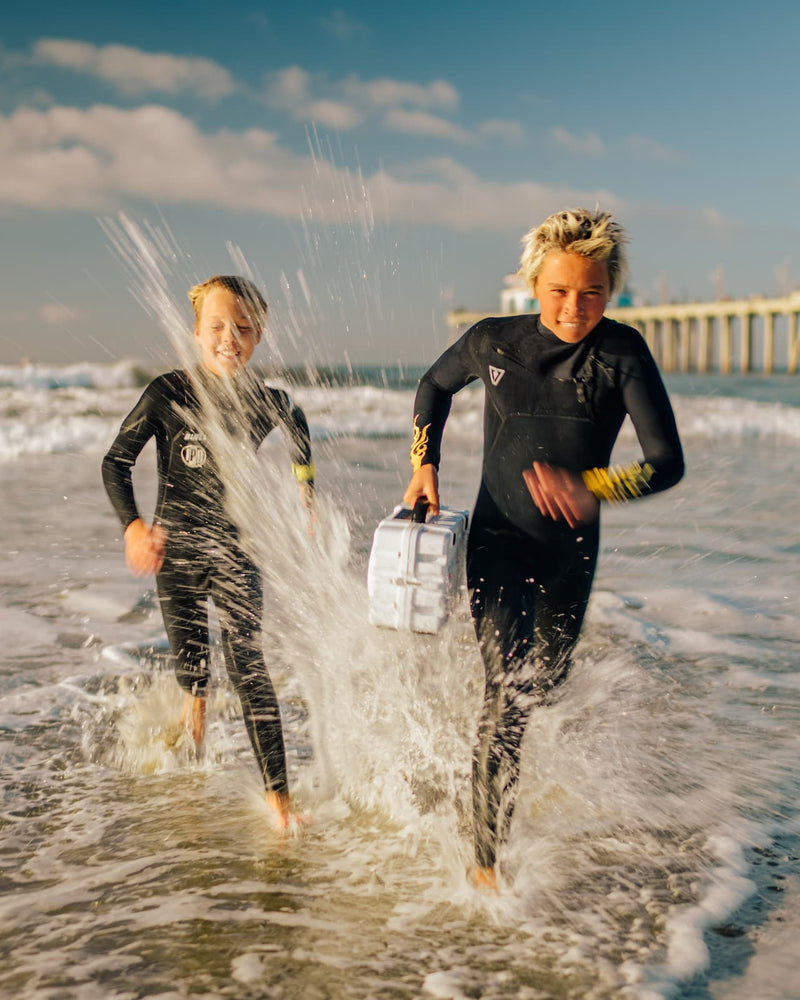 Two kids running on the beach with a Turtlebox Original speaker in his hand.