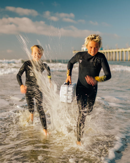 Two kids running on the beach with a Turtlebox Original speaker in his hand.