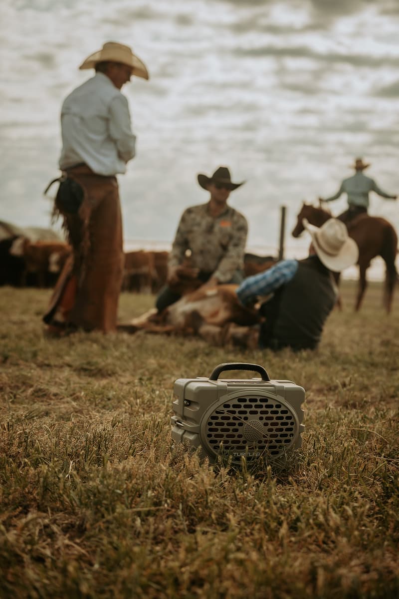 lifestyle photo showing some cowboys in a field, with a Tan speaker in the foreground  #speaker-color_tan