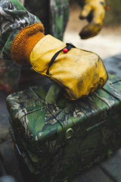 A macro shot of a guy carrying his Mossy Oak Full Foliage Turtlebox speaker with his yellow glove