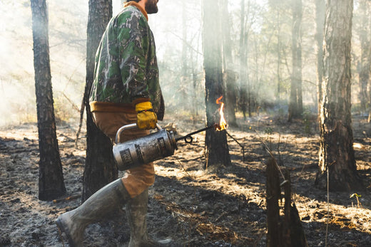 Guy is walking in a forest and is carrying a gasoline lighter on his right hand