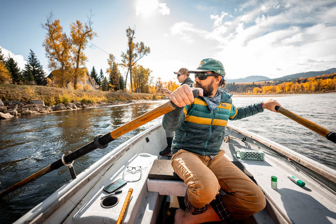Two guys in a boat, rowing and fishing with a Turtlebox Ranger speaker in River Rock color