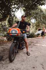 A lifestyle photo from Shane Dorian, our ambassador, driving a motorcycle and carrying a Turtlebox Original speaker in orange color tied up with the straps #speaker-color_orange