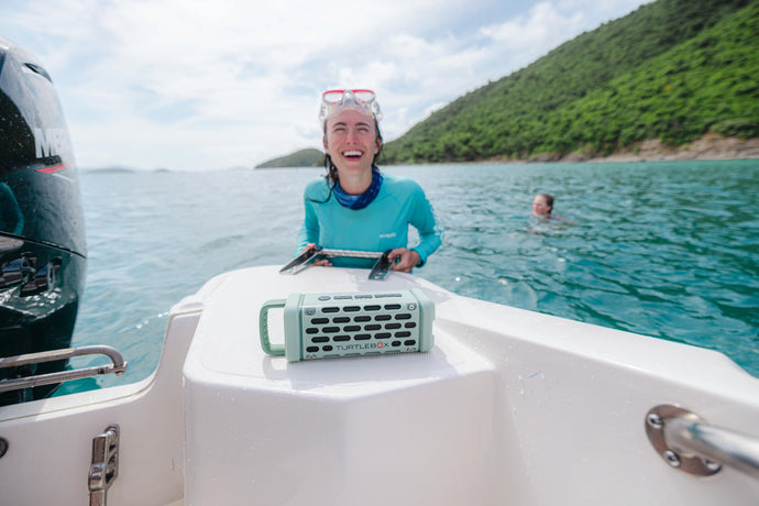 A girl climbing to the boat after doing snorkling, a Turtlebox Ranger speaker in River Rock color is playing on the boat.