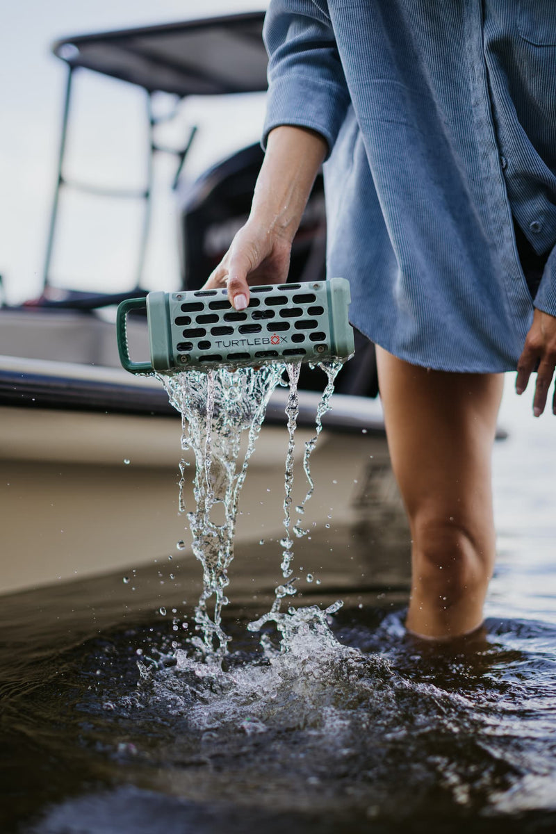 A lifestyle photo of a woman removing a Ranger speaker in River Rock from water close to the boat. #base-color_river-rock